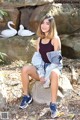 A woman sitting on a rock next to a white swan.