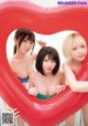 A group of three young women posing in front of a heart shaped balloon.