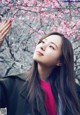 A woman with long brown hair standing in front of a flowering tree.