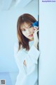 A woman in a white shirt leaning against a wall.
