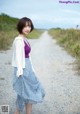 A woman standing on a dirt road next to a field.