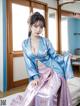 A woman in a blue and pink kimono sitting on a bed.